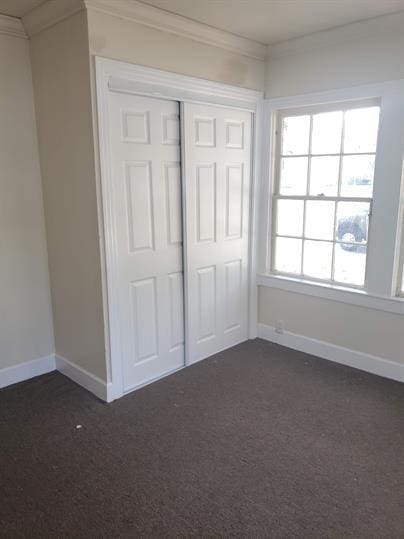 unfurnished bedroom featuring baseboards, dark colored carpet, a closet, and crown molding