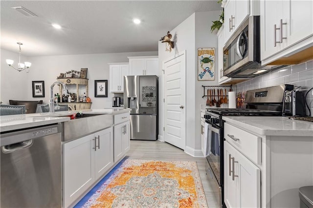 kitchen with appliances with stainless steel finishes, pendant lighting, tasteful backsplash, sink, and white cabinets