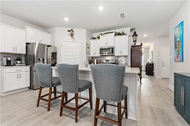 kitchen featuring a kitchen island with sink, stainless steel appliances, a kitchen breakfast bar, and white cabinets