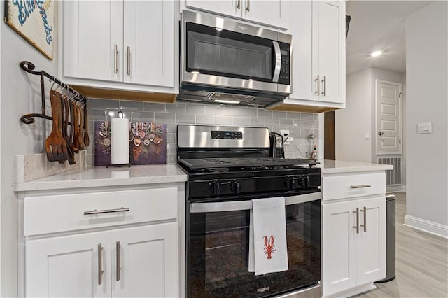 kitchen featuring white cabinetry, stainless steel appliances, light wood-type flooring, and backsplash