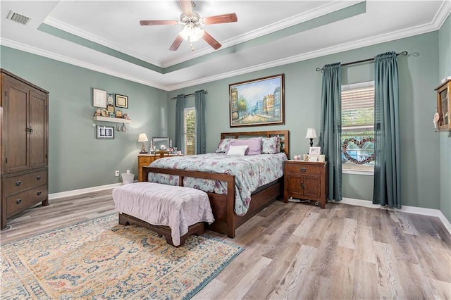 bedroom featuring multiple windows, light wood-type flooring, ceiling fan, and a raised ceiling