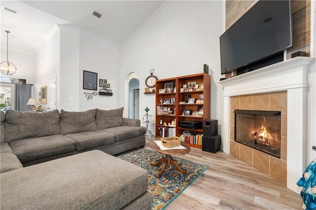 living room featuring light hardwood / wood-style flooring, high vaulted ceiling, ornamental molding, a tiled fireplace, and a chandelier