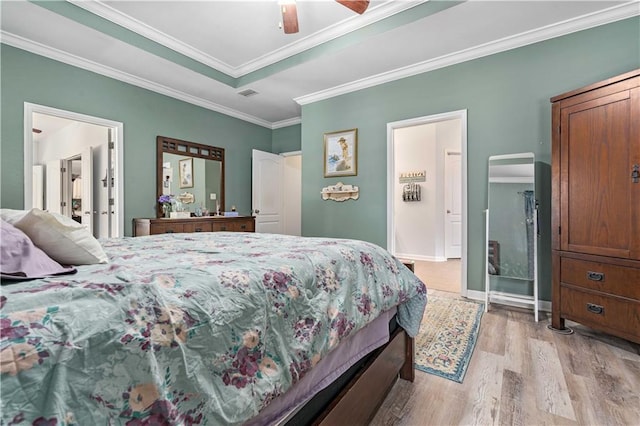 bedroom with connected bathroom, ceiling fan, a raised ceiling, crown molding, and light wood-type flooring