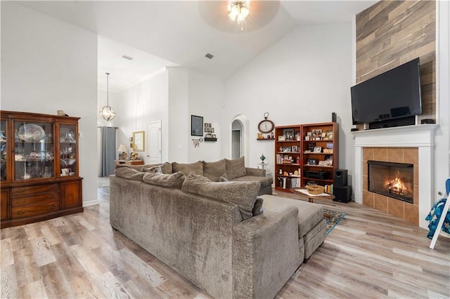 living room featuring a fireplace, light hardwood / wood-style flooring, high vaulted ceiling, and ceiling fan