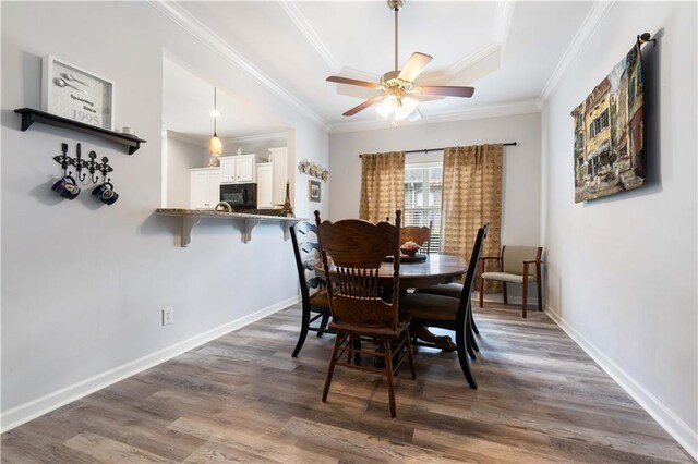 dining space with hardwood / wood-style flooring, a tray ceiling, ornamental molding, and ceiling fan