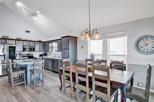 dining area featuring visible vents, light wood-style flooring, rail lighting, an inviting chandelier, and high vaulted ceiling