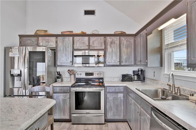 kitchen featuring visible vents, a sink, appliances with stainless steel finishes, light countertops, and vaulted ceiling