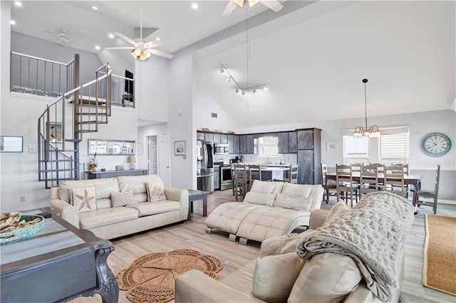 living area featuring stairway, light wood finished floors, high vaulted ceiling, recessed lighting, and ceiling fan with notable chandelier