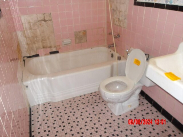 bathroom with tile walls, tile patterned flooring, toilet, and shower / washtub combination