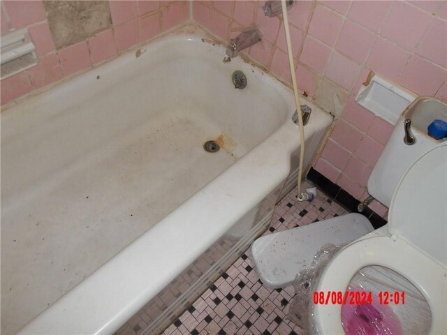 bathroom with tile walls, a bath, toilet, and tile patterned flooring