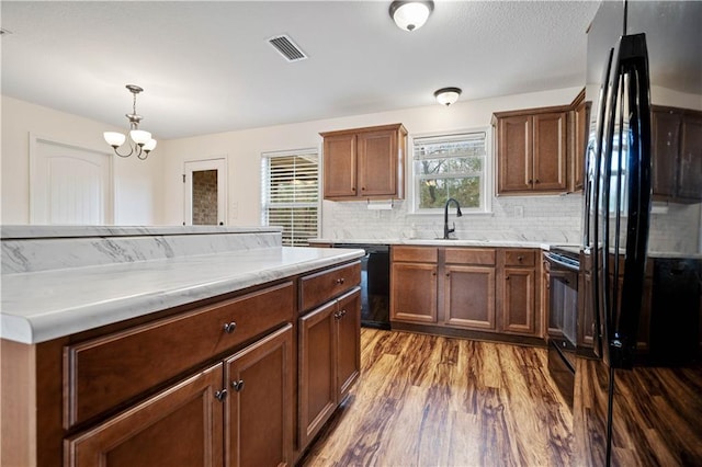 kitchen featuring hardwood / wood-style floors, decorative light fixtures, sink, backsplash, and black appliances