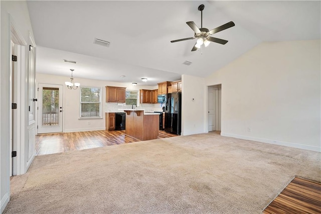 kitchen with ceiling fan with notable chandelier, black appliances, a kitchen island, decorative light fixtures, and light colored carpet