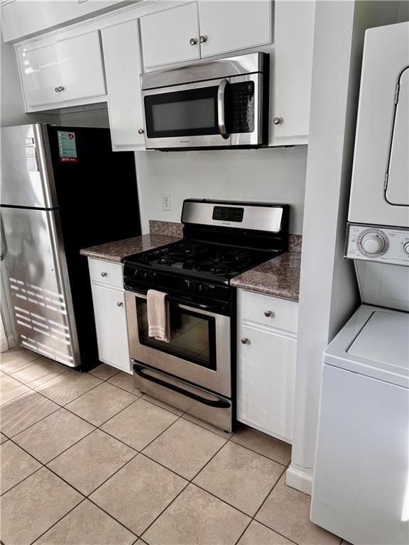 kitchen featuring white cabinetry, light tile patterned flooring, stainless steel appliances, and stacked washer / drying machine