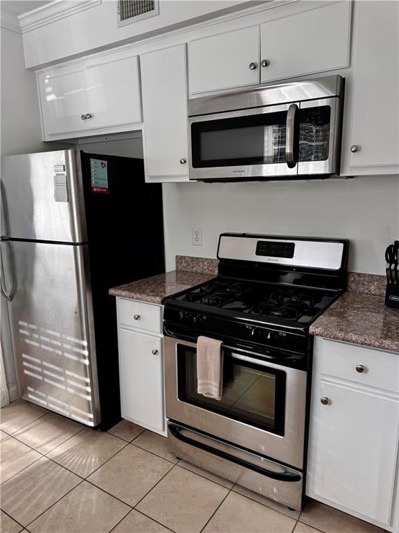 kitchen with dark stone counters, stainless steel appliances, crown molding, white cabinetry, and light tile patterned flooring