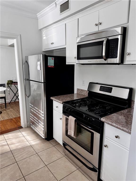 kitchen featuring white cabinetry, dark stone countertops, appliances with stainless steel finishes, light tile patterned floors, and ornamental molding