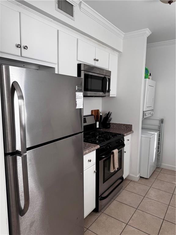 kitchen with appliances with stainless steel finishes, ornamental molding, light tile patterned floors, white cabinets, and stacked washer and dryer