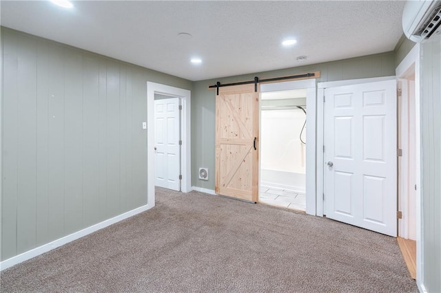 unfurnished bedroom featuring carpet, a barn door, and an AC wall unit