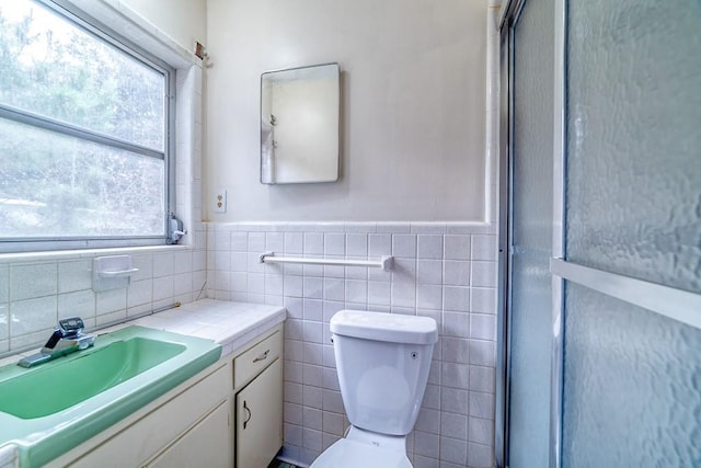 bathroom with a shower with door, vanity, tile walls, and toilet