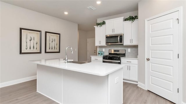 10676 Relic Rd N, Mobile, AL 36608 - kitchen with appliances with stainless steel finishes, light wood-style flooring, a center island with sink, light countertops, and decorative backsplash