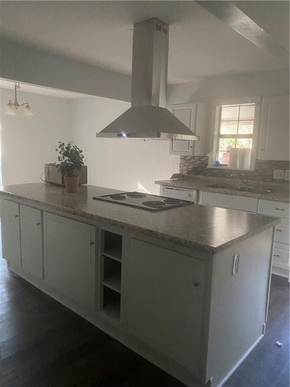 kitchen with white cabinets, a center island, stainless steel stovetop, and wall chimney range hood