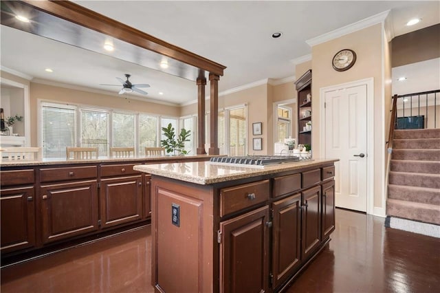 kitchen with light stone countertops, a kitchen island, ceiling fan, and crown molding