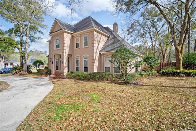 view of front of house with a front yard, fence, stucco siding, a chimney, and concrete driveway