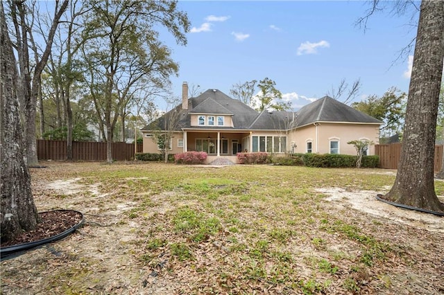 rear view of property featuring a yard, stucco siding, a chimney, and fence