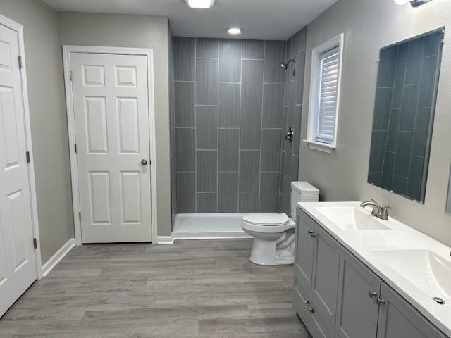 bathroom with a tile shower, hardwood / wood-style flooring, toilet, and vanity