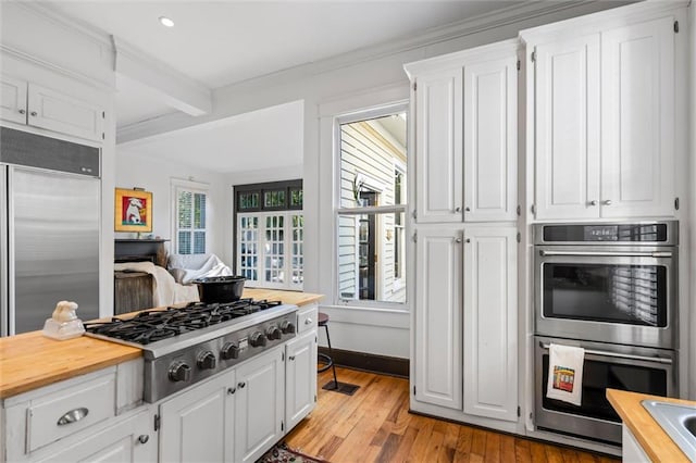 kitchen with stainless steel appliances, white cabinetry, crown molding, and light hardwood / wood-style flooring