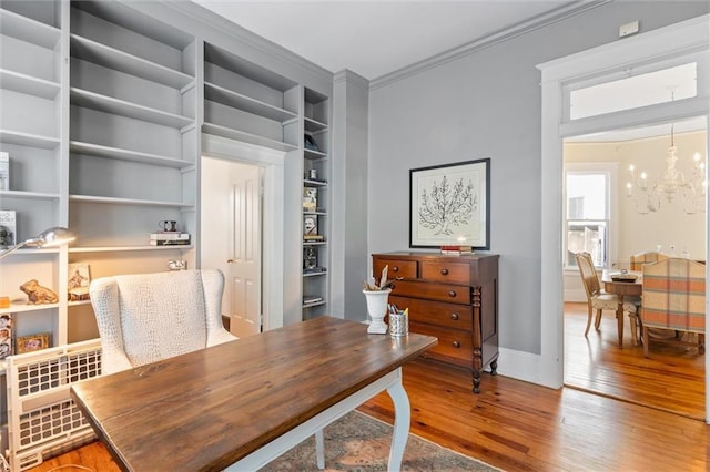 office with hardwood / wood-style floors, built in shelves, ornamental molding, and a chandelier