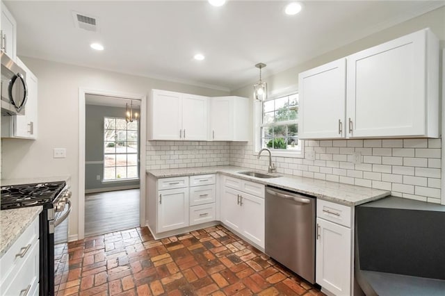 kitchen featuring backsplash, sink, appliances with stainless steel finishes, decorative light fixtures, and white cabinetry