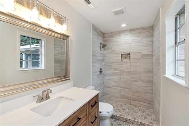 bathroom with a tile shower, vanity, and toilet