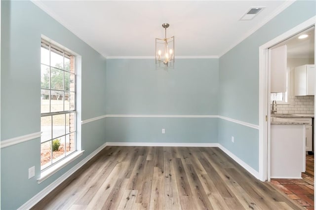 unfurnished dining area featuring a chandelier, crown molding, a wealth of natural light, and light hardwood / wood-style flooring