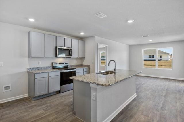 kitchen with sink, gray cabinetry, an island with sink, stainless steel appliances, and light stone countertops