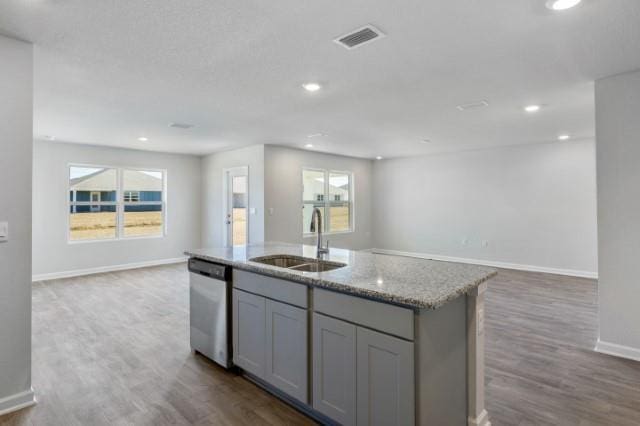 kitchen with gray cabinets, sink, a kitchen island with sink, stainless steel dishwasher, and light stone countertops