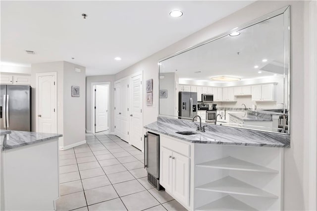 kitchen with sink, white cabinets, light stone counters, kitchen peninsula, and stainless steel appliances