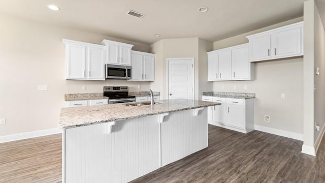 kitchen with sink, appliances with stainless steel finishes, light stone countertops, an island with sink, and white cabinets