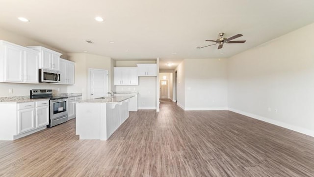 kitchen featuring white cabinetry, light stone counters, wood-type flooring, a center island with sink, and stainless steel appliances