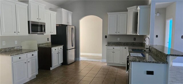 2509 Hedgerow Dr, Mobile, AL 36695 - kitchen with dark stone countertops, a sink, arched walkways, a peninsula, and appliances with stainless steel finishes