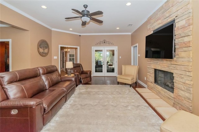 living room with a stone fireplace, crown molding, recessed lighting, and french doors