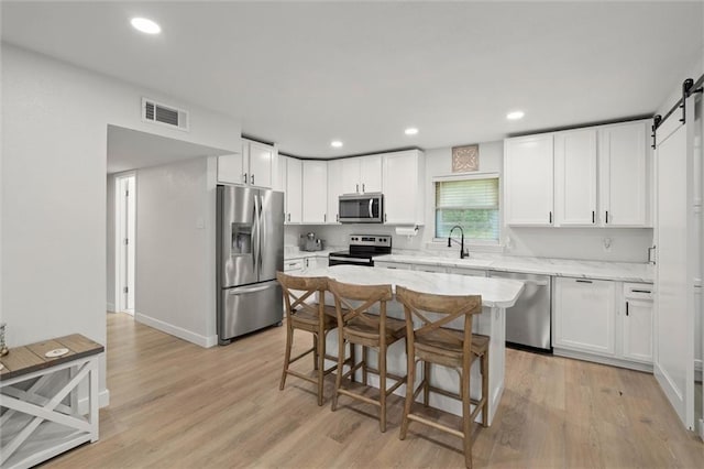 254 Fairford Rd, Calvert, AL 36513 - kitchen with appliances with stainless steel finishes, a barn door, white cabinetry, light wood finished floors, and recessed lighting