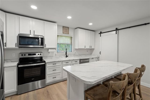 254 Fairford Rd, Calvert, AL 36513 - kitchen with appliances with stainless steel finishes, light wood finished floors, a barn door, white cabinets, and recessed lighting