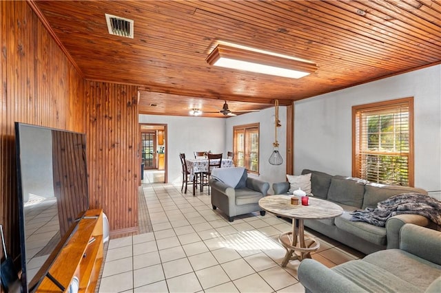 tiled living room with a skylight, ceiling fan, wooden ceiling, and wood walls