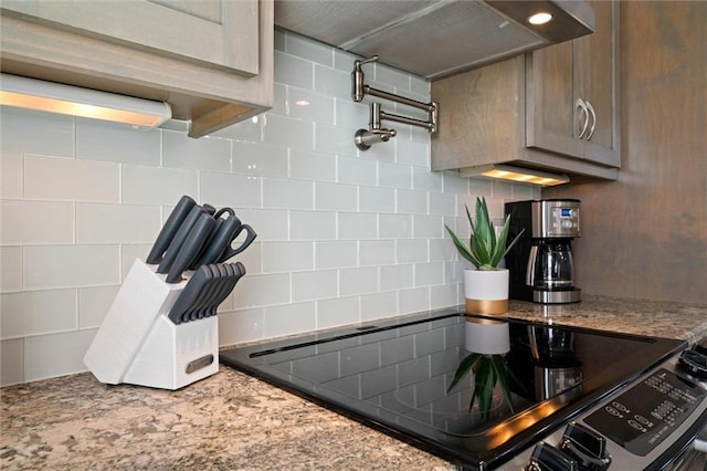 kitchen with decorative backsplash, range, light stone counters, and wall chimney range hood