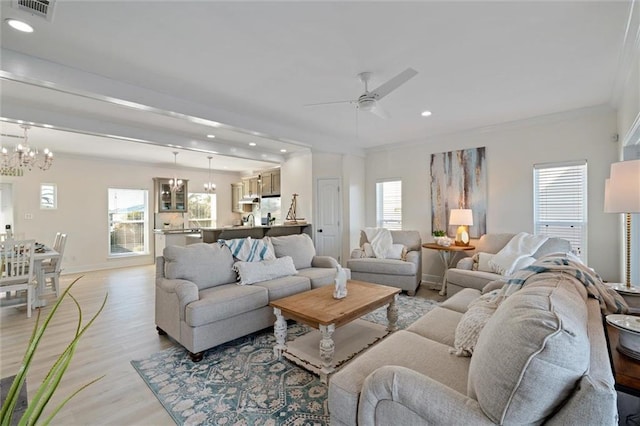 living room with ceiling fan with notable chandelier, light wood-type flooring, and ornamental molding