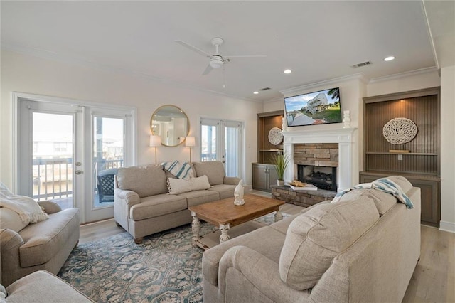 living room featuring ceiling fan, light wood-type flooring, a fireplace, and ornamental molding