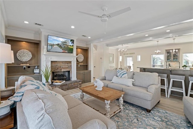 living room featuring ceiling fan with notable chandelier, light hardwood / wood-style flooring, a stone fireplace, and ornamental molding