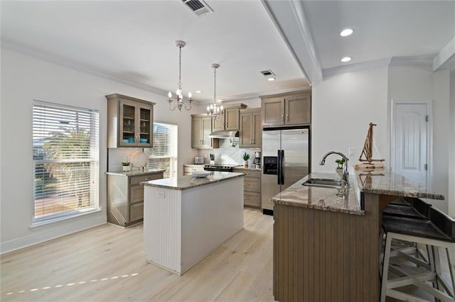 kitchen featuring appliances with stainless steel finishes, light stone counters, sink, pendant lighting, and a center island with sink