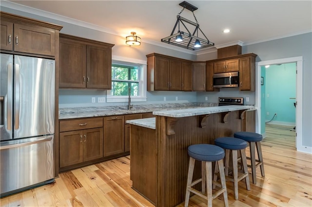 kitchen with stainless steel appliances, a center island, decorative light fixtures, light wood-type flooring, and light stone counters