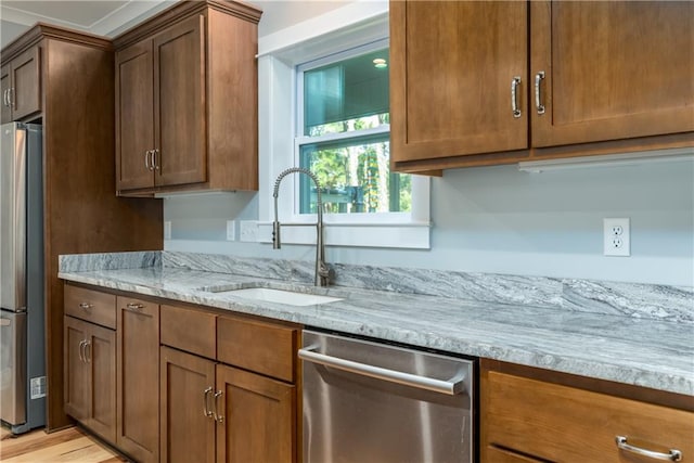 kitchen with light stone counters, appliances with stainless steel finishes, sink, and light wood-type flooring